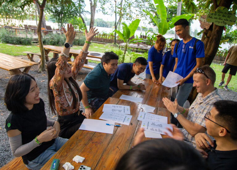 Corporate team building group discussion at outdoor table with facilitator and documents.
